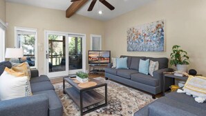 A living room with a sofa, coffee table, and a TV. There is a ceiling fan, a painting, and a plant. - Historic Happy Home Steps from Main Street w Private Yard, Screened-In Porch & Parking (Annapolis)