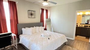 A bedroom with a bed, a ceiling fan, a bedside table, a chair, a rug, and a bathroom with a mirror and sink. - Monthly Stays Luxe Des Peres Suite with Complimentary Starbucks Onsite!  (Des Peres)
