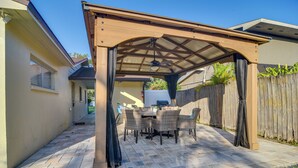 Ein überdachter Patio-Bereich mit Tisch und Stühlen, einem Deckenventilator und einem Holzzaun im Hintergrund.