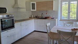 Ett modernt kök med vita skåp, en inbyggd ugn, en diskho och en matplats med ett bord och stolar.