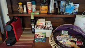 Ett köksutrymme med en kaffemaskin, en flaska olivolja, en förpackning pasta och en korg med snacks.