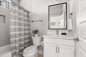Une salle de bain avec des toilettes blanches, un lavabo surmonté d’un miroir et un rideau de douche à rayures horizontales.