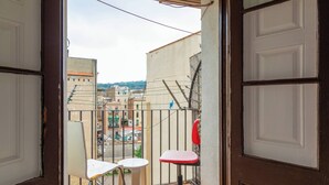 Un balcon avec deux chaises et une petite table, d’où l’on peut admirer un paysage urbain avec ses bâtiments et un ciel dégagé.