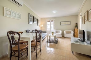 A living room with a dining table, chairs, a sofa, a TV, and a coffee table.