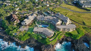 Vista aérea de um resort costeiro com vários edifícios, uma piscina e um litoral rochoso.