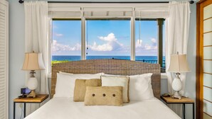 Quarto com uma cama grande, duas mesas de cabeceira, um relógio digital e vista para o oceano.