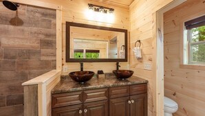 Une salle de bain rustique, avec des murs en bois, équipée d’un double lavabo, d’un grand miroir et d’une douche.
