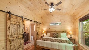 Une chambre dans une cabane en bois, avec un lit, deux lampes de chevet, un ventilateur de plafond et une fenêtre.