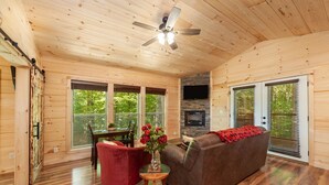 L’intérieur d’un chalet accueillant, avec un plafond en bois, une cheminée, un canapé, un fauteuil rouge et une table à manger.