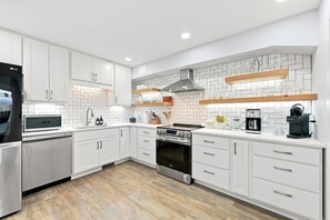 A modern kitchen with white cabinetry, a built-in oven, a microwave, and a coffee machine.