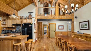Une cuisine spacieuse dotée de meubles en bois, d’un réfrigérateur noir et d’un coin repas avec des tables et des chaises en bois.