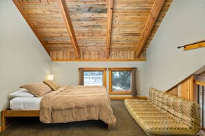 Un dormitorio con techo de madera, una cama, un sofá y dos ventanas.