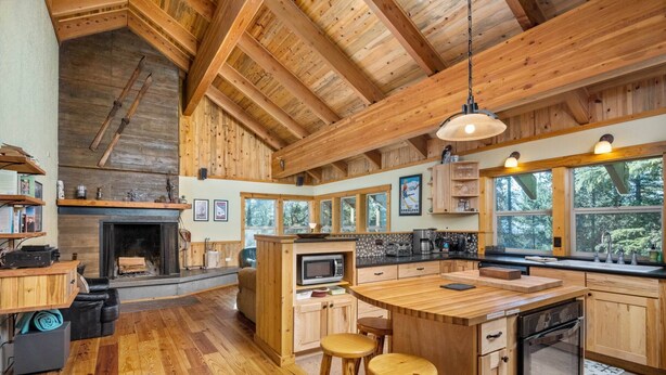 Une cuisine spacieuse avec des meubles en bois, un îlot central doté de tabourets, un four encastré et une grande fenêtre offrant une vue sur l’extérieur.