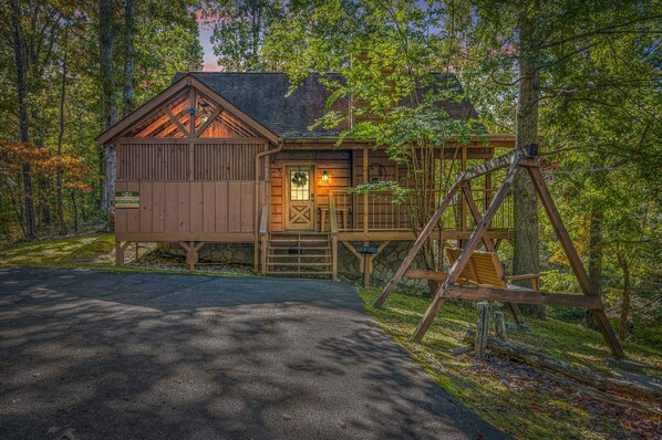 Relax on the porch with a swing and a bench, surrounded by a serene forest setting.