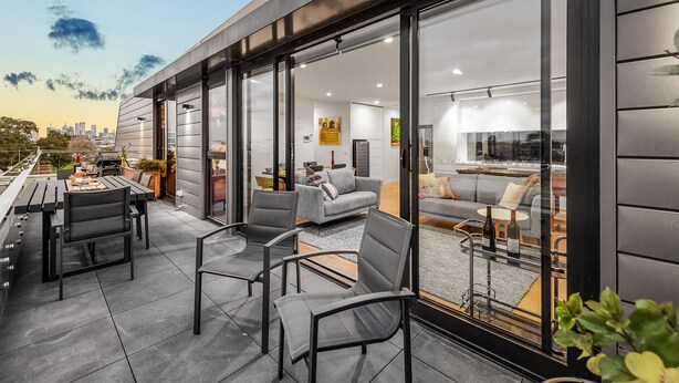 A modern outdoor patio with a dining area, seating, and a city view. - StayCentral - East Brunswick Penthouse with Study (Brunswick East)