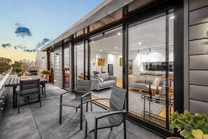 A modern outdoor patio with a dining area, seating, and a city view. - StayCentral - East Brunswick Penthouse with Study (Brunswick East)