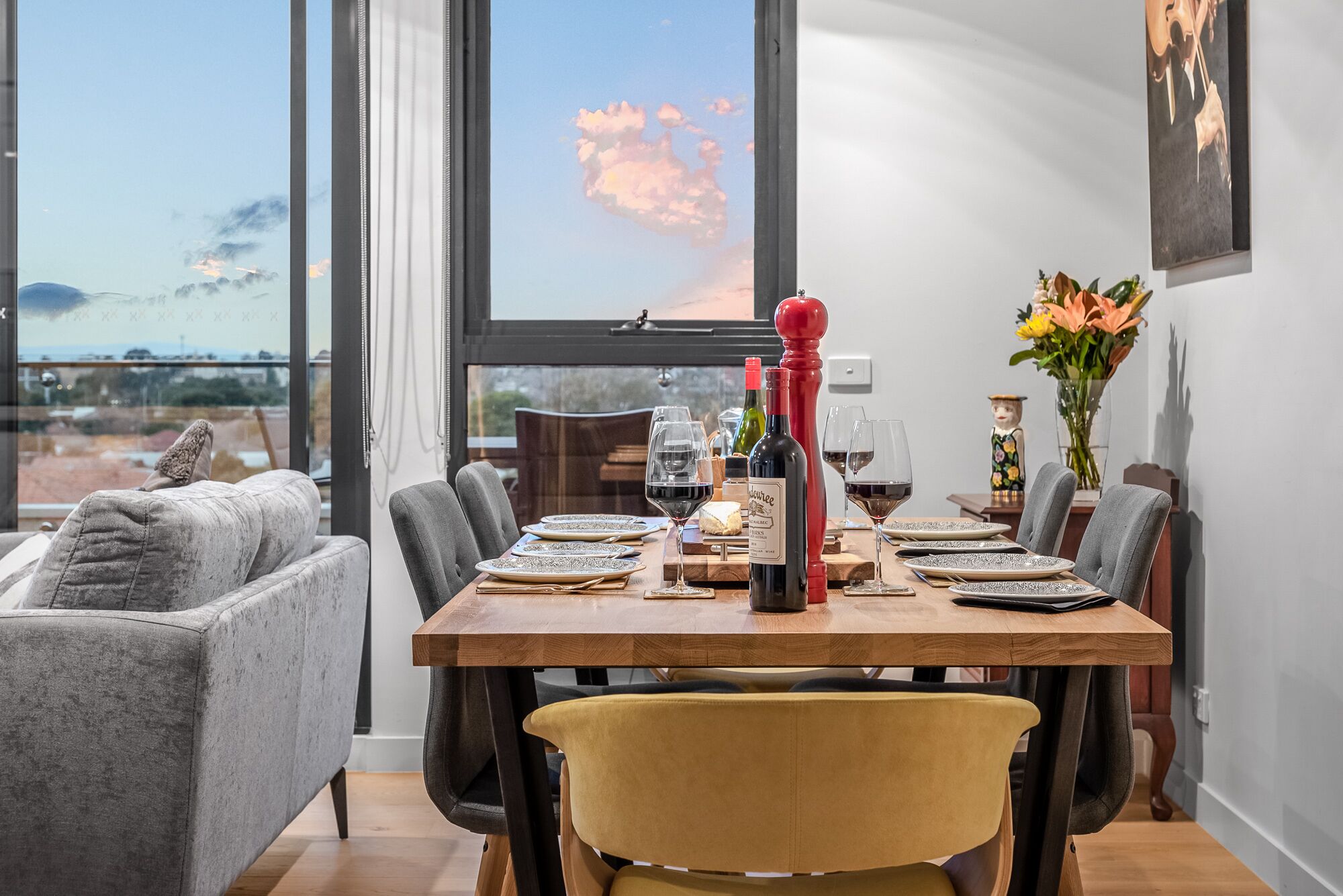 A dining table set for six with wine glasses, a bottle of wine, and a cheese platter.
