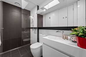 A modern bathroom with a glass-enclosed shower, a white toilet, and a vanity with a large mirror.