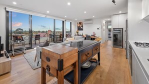 A modern kitchen with a large island, a dining area with a view, and a spacious living area with a sofa and a table. - StayCentral - East Brunswick Penthouse with Study (Brunswick East)