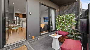 A modern outdoor patio area with a dining table, red cushioned seating, and a decorative plant wall. - StayCentral - Boulevard Gardens (Coburg)