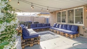 Un área de estar al aire libre con bancos acolchados azules y una mesa de madera, bajo un toldo a rayas.