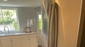 Una cocina con refrigerador de acero inoxidable, piso de madera y ventana con vista a espacios verdes.