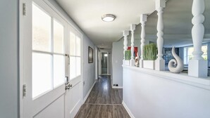 Un pasillo con paredes blancas, piso de madera y una escalera con barandilla de madera blanca.