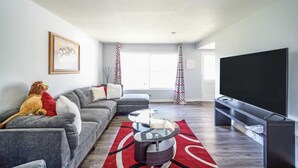 Una sala de estar moderna con un sofá seccional gris, una mesa de centro de vidrio, un televisor de pantalla plana y una alfombra roja.