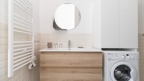 Un baño moderno con lavamanos blanco, espejo y lavadora integrada.