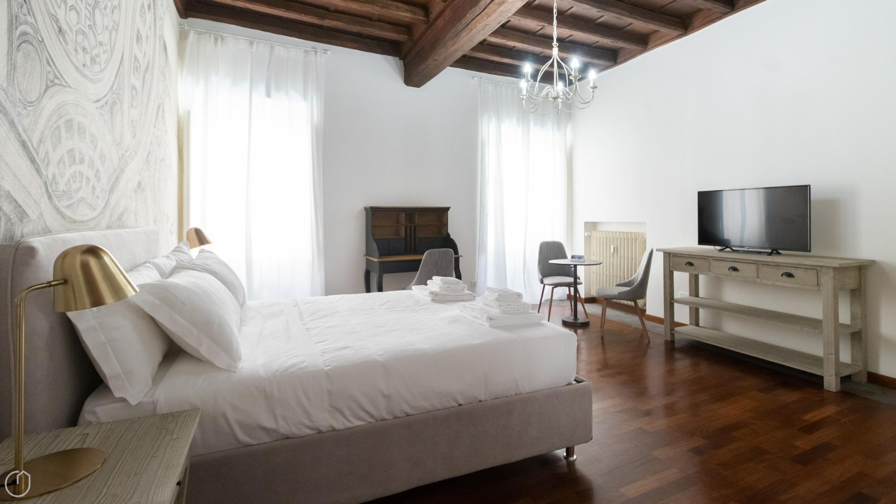 A modern hotel room with a large bed, a desk, a television, and a chandelier.