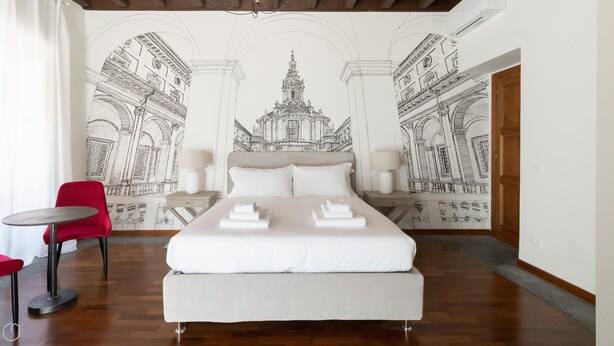 A hotel room with a large bed, two bedside tables, a red chair, and a wall mural of architectural drawings.