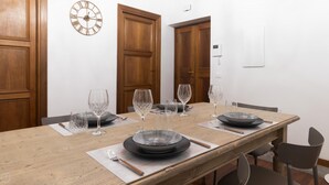 A dining table set with plates, glasses, and cutlery, flanked by wooden doors and a wall-mounted clock.