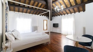 A bedroom with a four-poster bed, a round dining table, a TV, and a chandelier. - Italianway - Barberini 6 Opulentia (Rome)