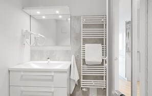 A modern bathroom with a white vanity, a towel rack, and a shower area. - Dünenvilla Superior (Lübeck)