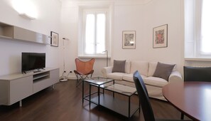 A modern living room with a flat-screen TV, a glass coffee table, a beige sofa, and a brown leather chair. - Italianway Easy - Vanvitelli 49 (Milan)