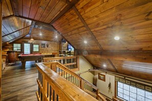A wooden interior with a pool table, a staircase, and a view of the outdoors. - Bent Pine Lodge | Spacious 4BR Broken Bow Cabin with Hot Tub, Fire Pit & Grill (Hochatown)