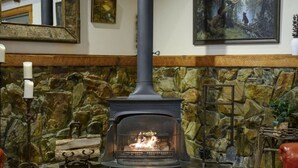 A stone fireplace with a black stove, a candle holder, and a painting on the wall. - Bent Pine Lodge | Spacious 4BR Broken Bow Cabin with Hot Tub, Fire Pit & Grill (Hochatown)