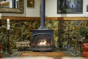 A stone fireplace with a black stove, a candle holder, and a painting on the wall. - Bent Pine Lodge | Spacious 4BR Broken Bow Cabin with Hot Tub, Fire Pit & Grill (Hochatown)