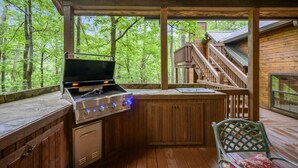 An outdoor kitchen with a grill and a sink, surrounded by wooden deck and a staircase leading to a covered area. - Bent Pine Lodge | Spacious 4BR Broken Bow Cabin with Hot Tub, Fire Pit & Grill (Hochatown)