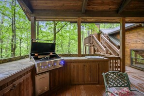 An outdoor kitchen with a grill and a sink, surrounded by wooden deck and a staircase leading to a covered area. - Bent Pine Lodge | Spacious 4BR Broken Bow Cabin with Hot Tub, Fire Pit & Grill (Hochatown)