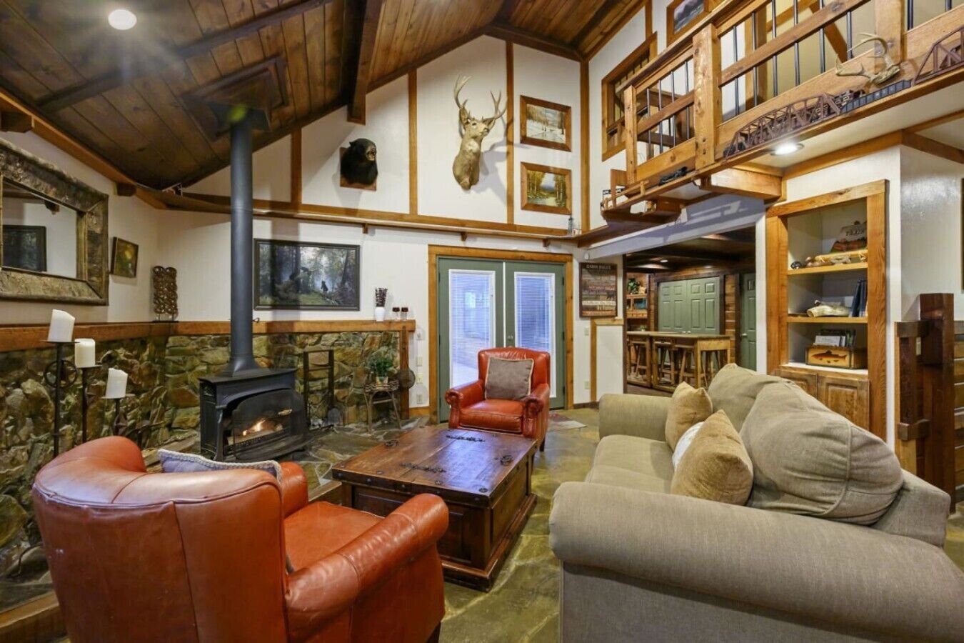 A cozy living room with a fireplace, leather chairs, a sofa, and a wooden ceiling.