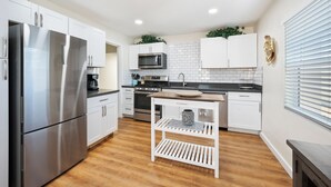 A modern kitchen with white cabinets, stainless steel appliances, and a wooden floor. - Townley on 6th! (Phoenix)