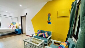 A modern living room with a yellow accent wall, a sofa set, a coffee table, and a bed. - goSTOPS PLUS Goa, Vagator (Vagator)