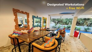 A modern dining area with a large wooden table, orange cushioned chairs, and colorful zigzag patterned pillows. - goSTOPS PLUS Goa, Vagator (Vagator)