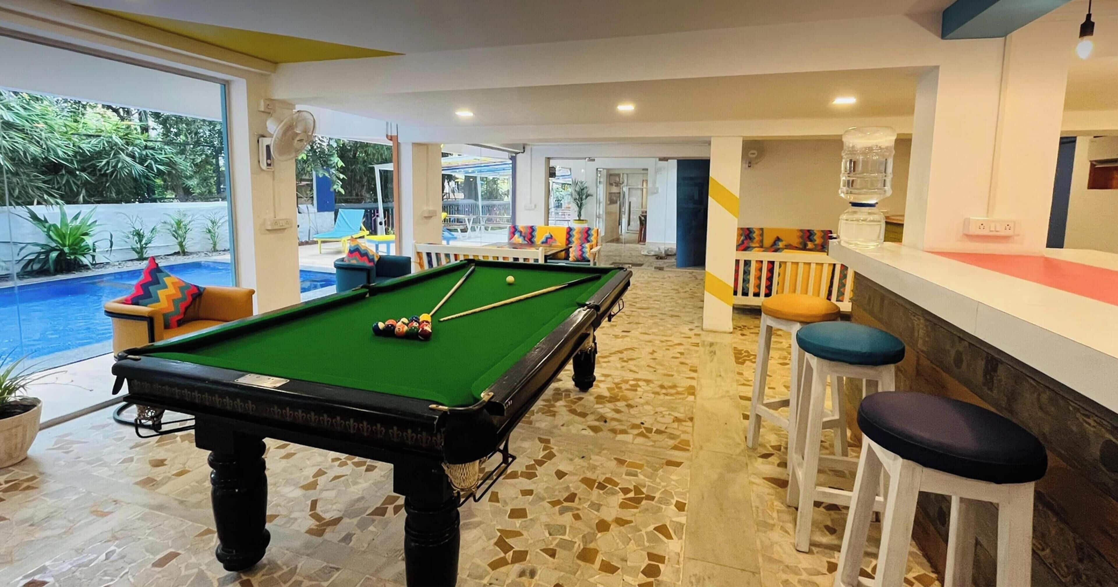 A pool area with a pool table, stools, and a bar.