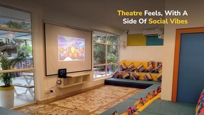 A theater with a projection screen, colorful seating, and a view of the outdoors. - goSTOPS PLUS Goa, Vagator (Vagator)