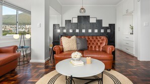 Ein modernes Wohnzimmer mit einem Ledersofa, einem runden Couchtisch mit Büchern und einer Vase, einer Zierwandverkleidung und Blick auf eine Stadtlandschaft durch große Fenster.