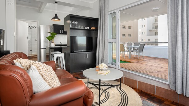 Ein modernes Wohnzimmer mit einem braunen Ledersofa, einem runden Couchtisch und Blick auf einen Balkon mit Gartenmöbeln.