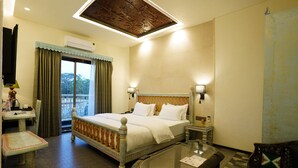 A hotel room with a bed, bedside tables, a glass table, a chair, and a view of the outdoors. - The Kinara Village (Mawal)