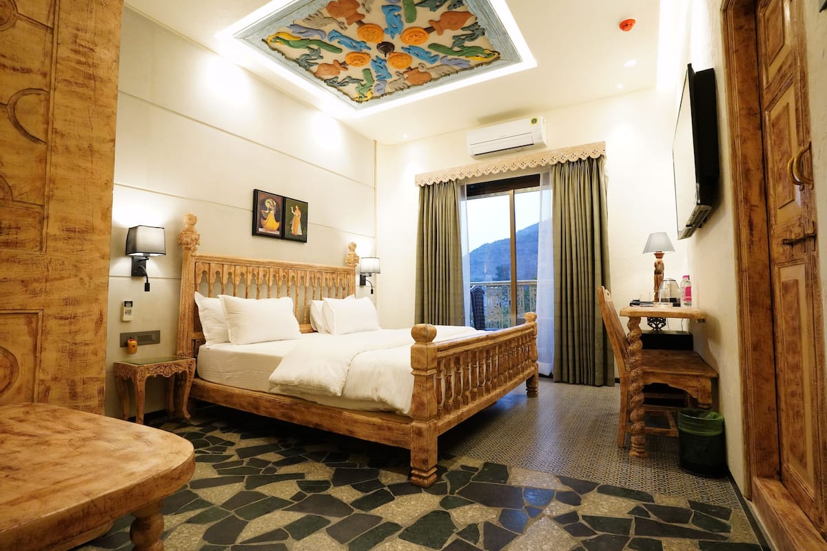 A room with a bed, a wooden table, a desk, a chair, a ceiling with a fish mural, and a window with curtains.